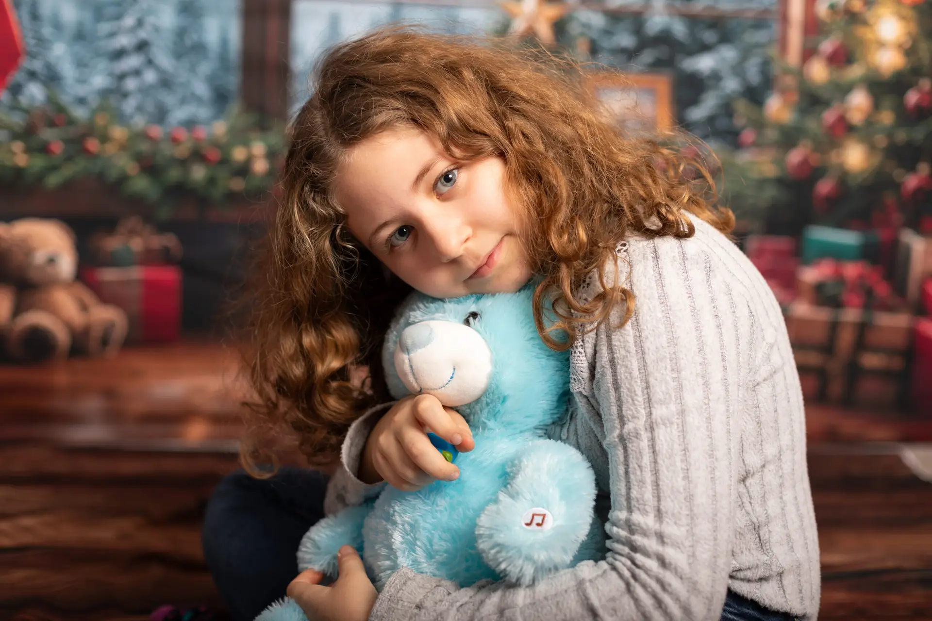 Enfant faisant un câlin a un doudou devant un decors de Noël , son regard plongeant dans le regard du photographe